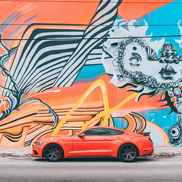 Raízes, blues e cores do sul. Imagem de muro pintado com gravuras coloridas e carro vermelhor - ferrari - na frente do muro.